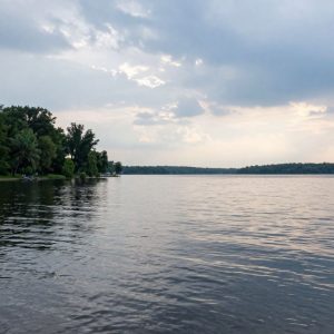 A tranquil evening scene of Lake Murray with tree-lined shores and cloudy skies.